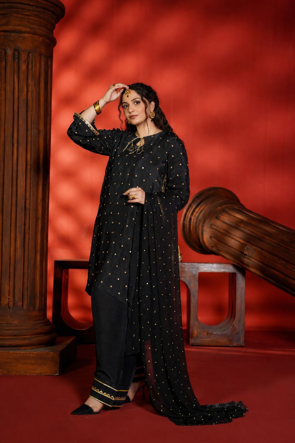 Woman in a black traditional outfit with gold details against a red background