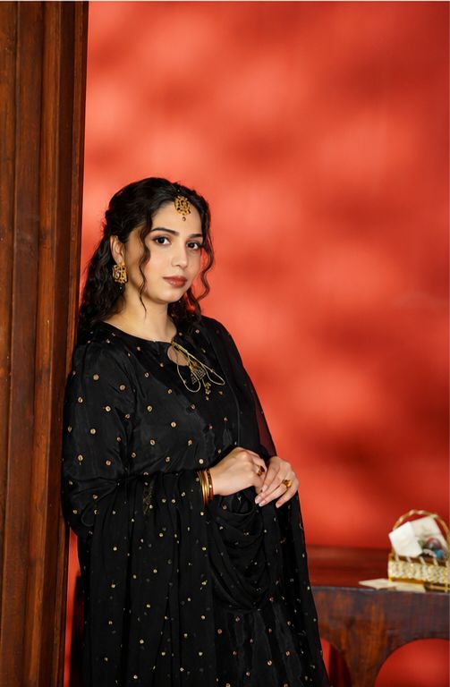 Woman in a black dress with gold details against a red wall.